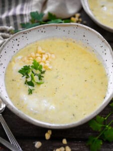 Two bowls of summer corn soup garnished with fresh parsley and a sprinkle of corn.