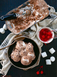 Overheard shot of Chocolate Marshmallow Swirl Ice Cream in a bowl and serving dish with cherries and marshmallows scattered around.