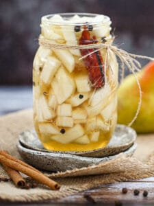 Quick Pickled Pears in a mason jar with cinnamon sticks and a pear in the background,