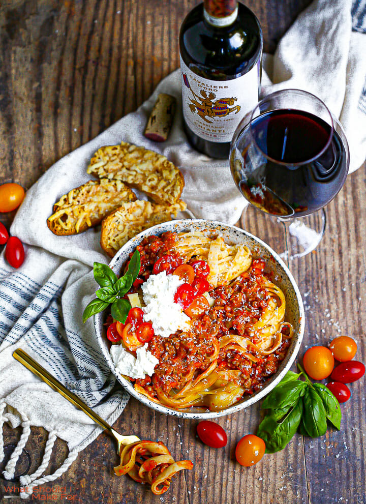 A bowl of fettuccine with bolognese sauce, fresh ricotta, and tomatoes served with parmesan crisps and Chianti.