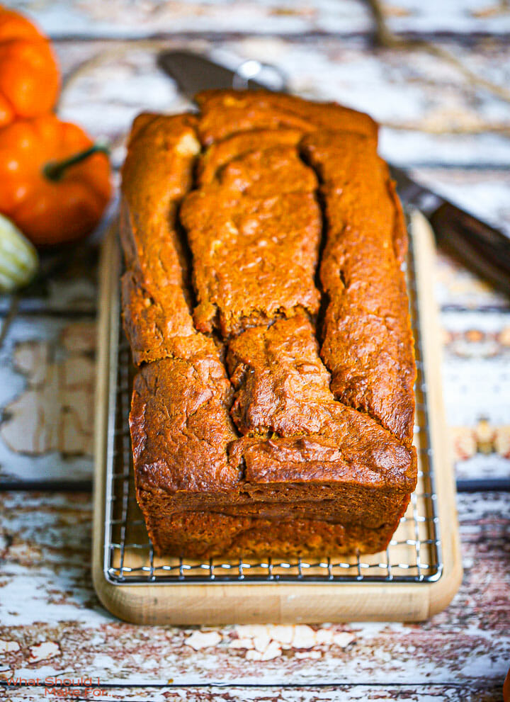 A loaf of pumpkin bread on a rack and cutting board with a knife in the background.