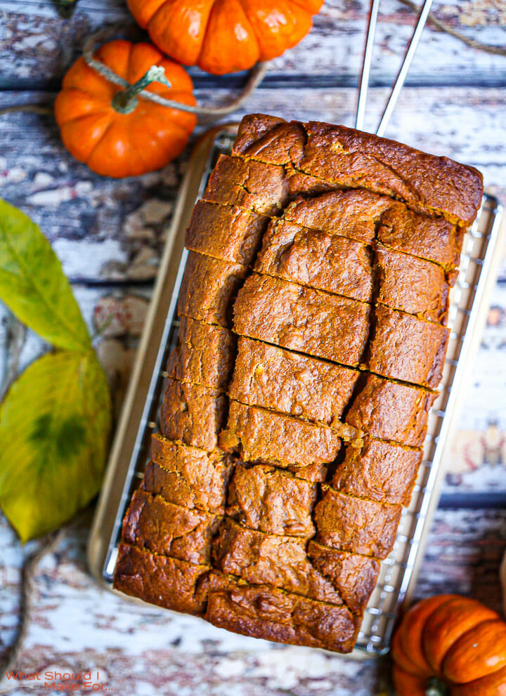 A sliced loaf of pumpkin bread on a cooling rack with pumpkins scattered around.