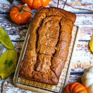 A sliced loaf of pumpkin bread on a cooling rack with pumpkins scattered around.