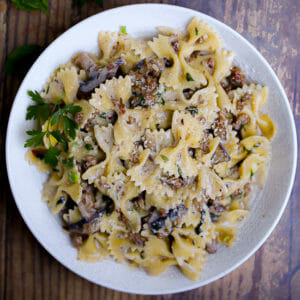 Close up of creamy farfalle pasta tossed with mushrooms and sausage in a creamy white wine sauce served in a white bowl.
