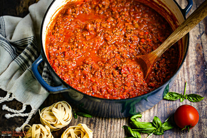 Bolognese Sauce in a dutch oven with fresh basil and nests of uncooked fettuccine on the table