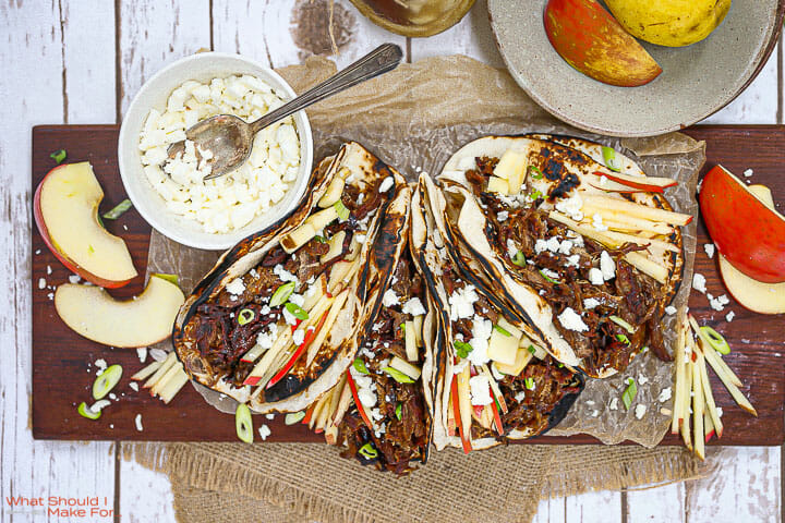 Slow Roasted Lamb Tacos on a wooden board with apples and feta cheese.