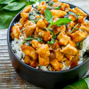 Thai Basil Chicken in a black bowl served over rice and garnished with basil.