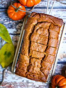 A sliced loaf of pumpkin bread on a cooling rack with pumpkins scattered around.