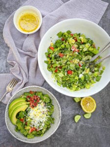 A serving of Chopped BLT Breakfast Salad next to the bowl, dressing and a gray napkin on the table.