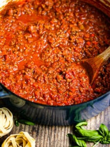 Bolognese Sauce in a dutch oven with fresh basil and nests of uncooked fettuccine on the table