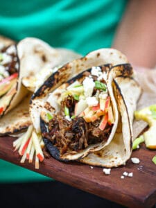 Someone holding Slow Roasted Lamb Tacos on a wood board.