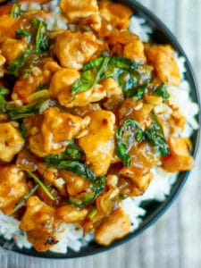 Close up of Thai Basil Chicken in a black bowl serve over rice.