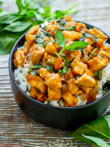 Thai Basil Chicken in a black bowl served over rice and garnished with basil.