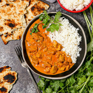 A bowl of Easy Butter Chicken served with rice, naan and cilantro.