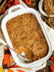 A scoop of Sweet Potato Soufflé removed from the baking dish with the serving spoon in the dish and flowers and nuts scattered around.