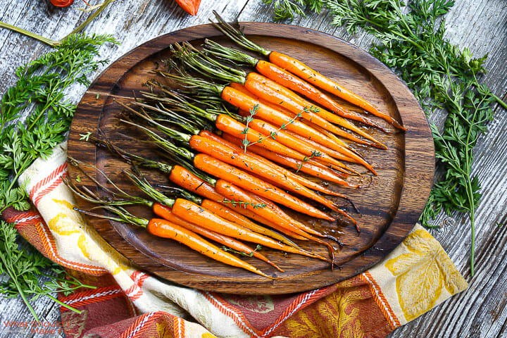 Honey Glazed Carrots on an oval serving tray on top of a festive linen with greens scattered around.