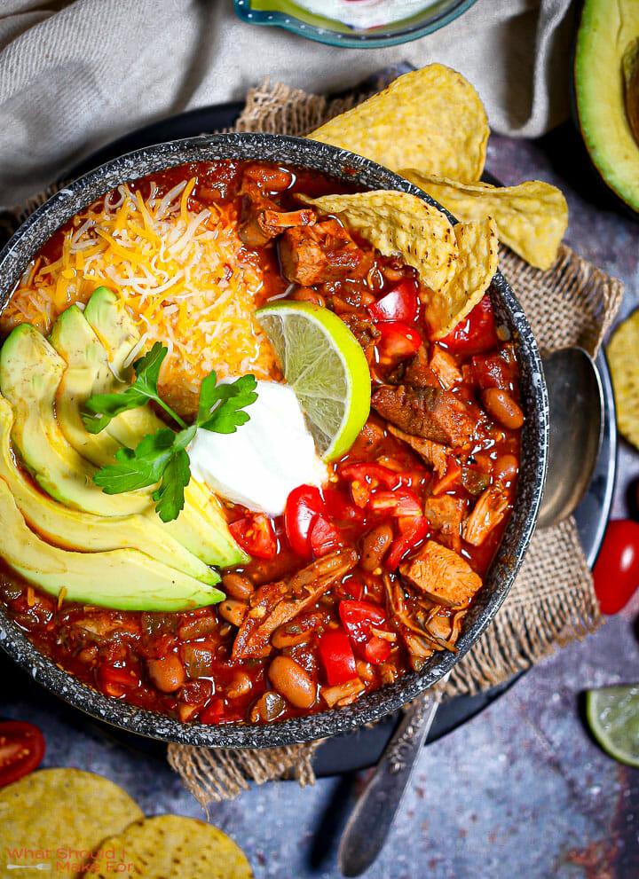 A bowl of Leftover Turkey Chili garnished with avocado, cheese, sour cream and limes.