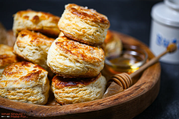 Close up of the best flaky biscuits with honey and butter in the background.