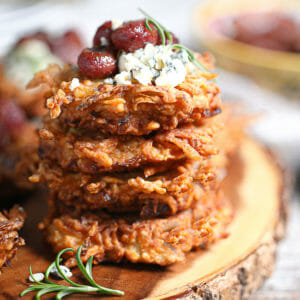 A stack of Potato Latkes with Gorgonzola and Roasted Red Grapes on a wood board.