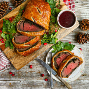 A sliced Beef Wellington with Red Wine Sauce on a cutting board with two slices on a small white plate.
