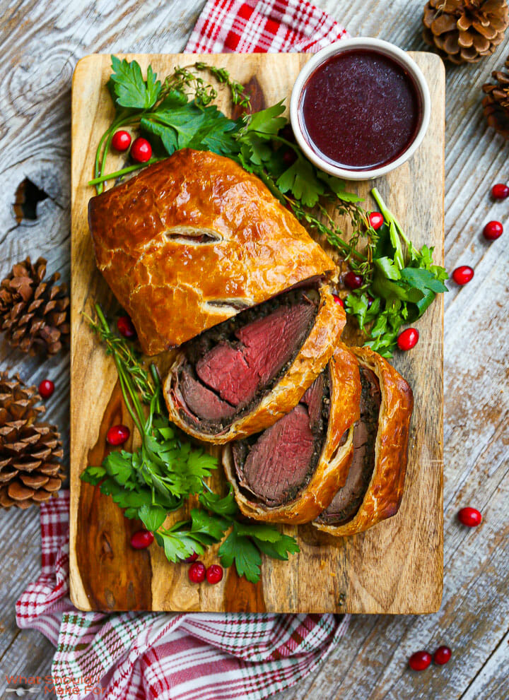 Overhead shot of Beef Wellington with Red Wine Sauce sliced on a cutting board with parsley scattered around.