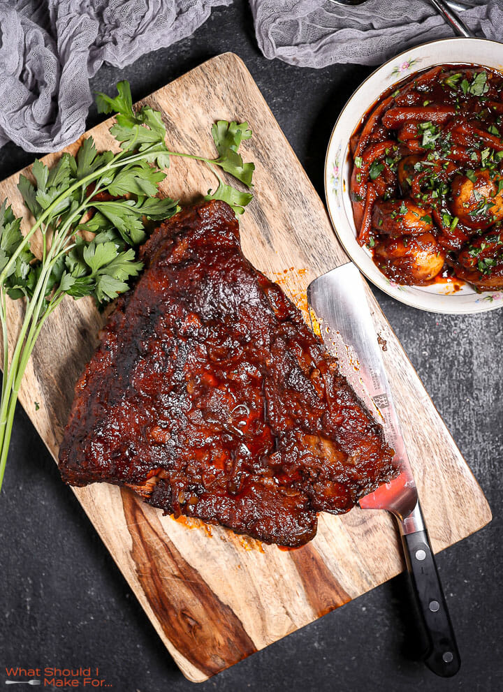 Best Sweet and Sour Brisket on a wood cutting board with a knife and parsely next to it.