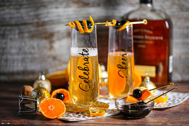 Bourbon Champagne Cocktails garnished with orange peel and cherries, with the garnishes scattered around.