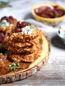 A stack of Potato Latkes with Gorgonzola and Roasted Red Grapes on a wood board.