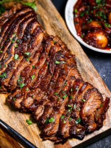 The Best Sweet and Sour Brisket on a wood board with potatoes and carrots on the side.