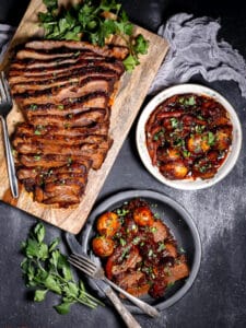 Overhead shot of the Best Sweet and Sour Brisket sliced on a boar, with potatoes on the side and a serving on a plate.