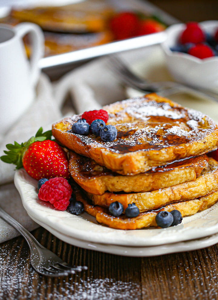 A serving of Brioche French Toast on a plate drizzled with syrup and served with berries.