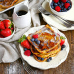 Brioche French Toast on a plate sprinkled with powdered sugar,drizzlwd with syrup and served with berries.