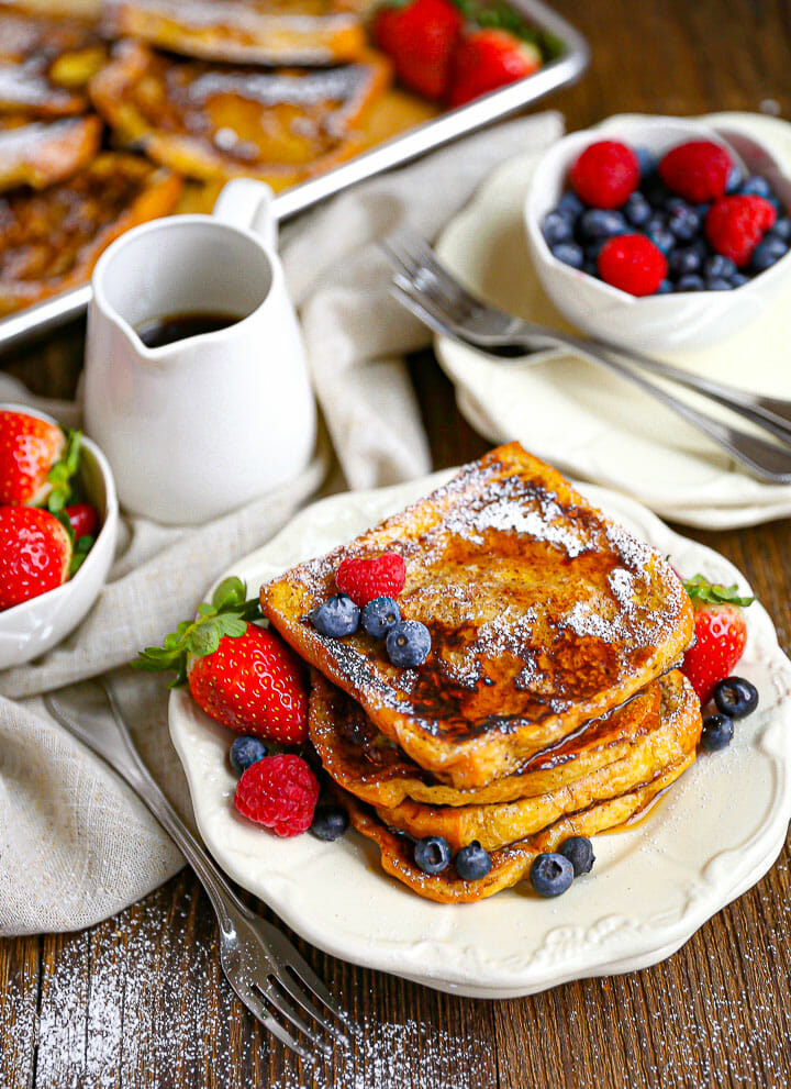 Brioche French Toast on a plate with a pitcher or syrup and sprinkled with berries.