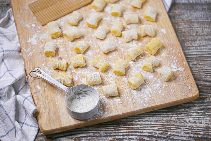 Potato gnocchi on a wood board with a measuring cup with flour.