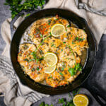 Chicken Piccata in a cast iron skilled garnished with lemon slices and parsley.