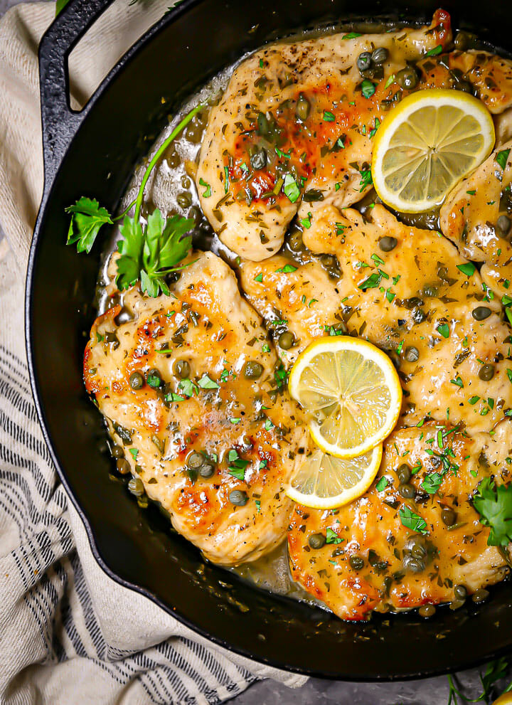Close up of chicken piccata garnished with lemon slices and capers.