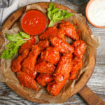 Baked Buffalo Wings on a serving tray with extra wing sauce, blue cheese and celery leaves.