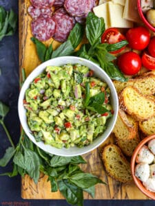 Overhead shot of Italian guacamole on a cheese board garnished with a sprig of basil.