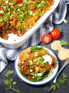 A serving of Beef Taco Casserole scooped out of the serving dish with a fork, chips and tomatoes scattered around.