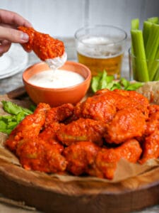 A hand dunking a baked buffalo wing into blue cheese.