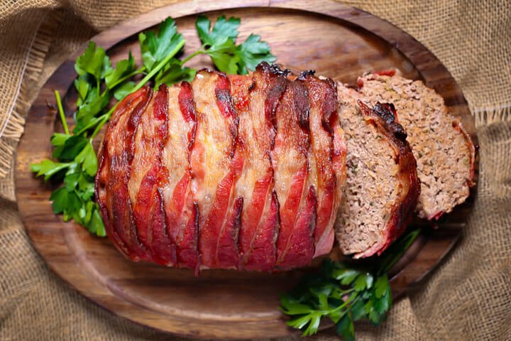 A bacon wrapped meatloaf on a tray with two slices cut.