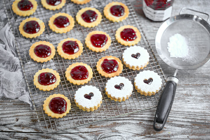 Linzer cookies being filled with raspberry jam and topped with a cut out cookie.