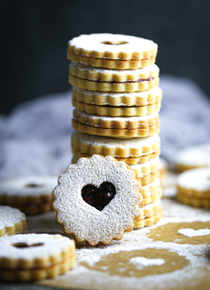 A stack of Nut-Free Linzer Cookies with one cookie with a heart shape cut out facing forward.