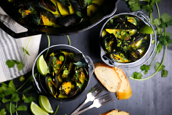 Two servings of Curry Coconut Mussels in small black crocks.