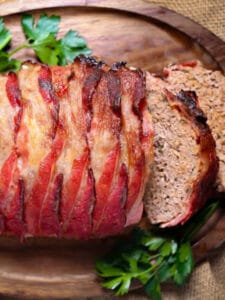 A bacon wrapped meatloaf on a tray with two slices cut.