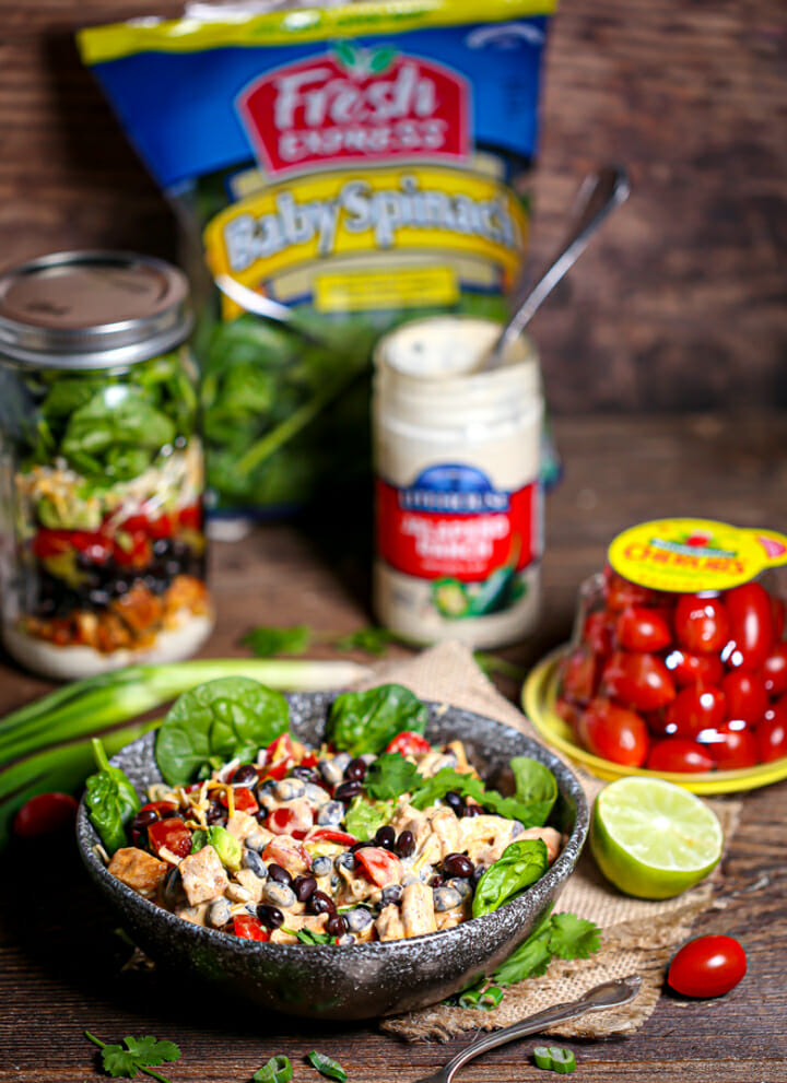 Layered Mexican Salad in a Jar in a serving bowl with all of the ingredients scattered around on the table.