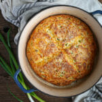 Cheddar and Scallion Soda Bread in a baking dish with scallions on the table.