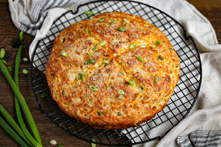 Cheddar and Scallion Soda Bread on a cooling rack scattered with scallions.