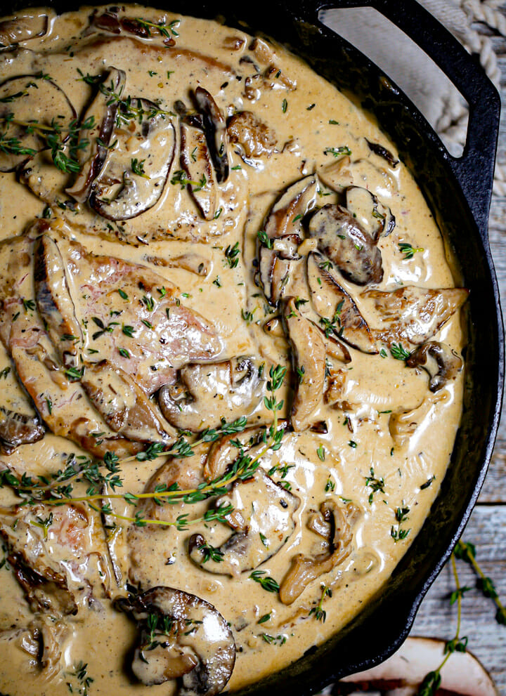 Close up of pork chops in a rich sauce with mushrooms and thyme.