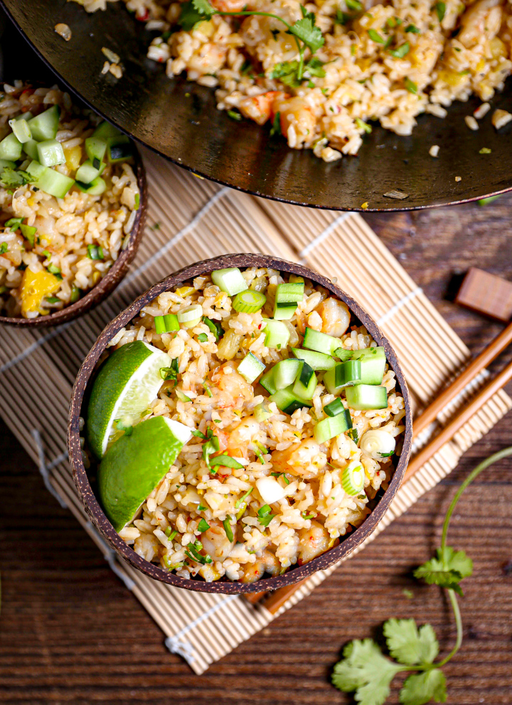 A bowl of shrimp fried rice garnished with lime wedges and diced cucumber.